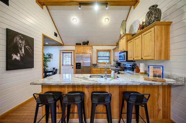 kitchen with appliances with stainless steel finishes, lofted ceiling with beams, sink, kitchen peninsula, and light brown cabinets