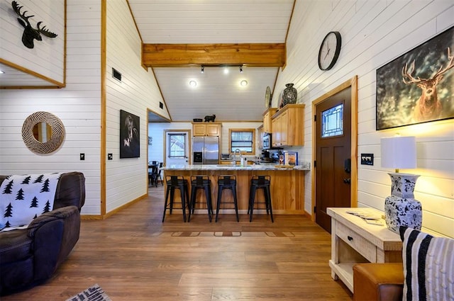 kitchen with a kitchen bar, appliances with stainless steel finishes, dark hardwood / wood-style floors, kitchen peninsula, and beamed ceiling