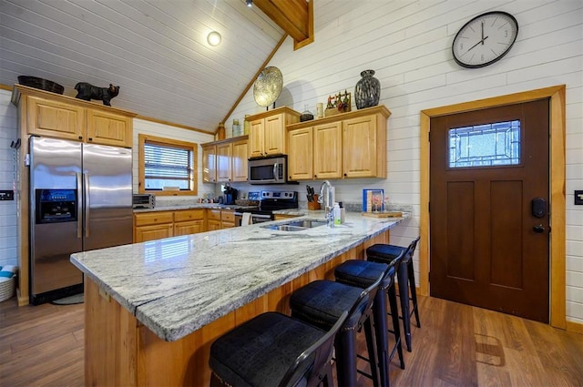 kitchen with sink, vaulted ceiling with beams, appliances with stainless steel finishes, a kitchen breakfast bar, and dark hardwood / wood-style flooring