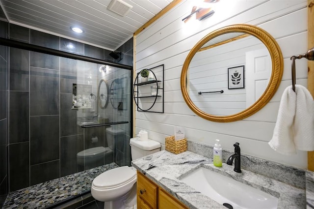 bathroom with vanity, wooden walls, a shower with door, and toilet