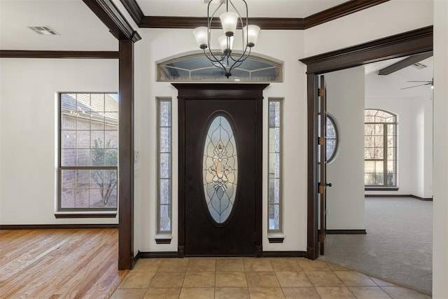 foyer with ornamental molding, ceiling fan with notable chandelier, and light carpet