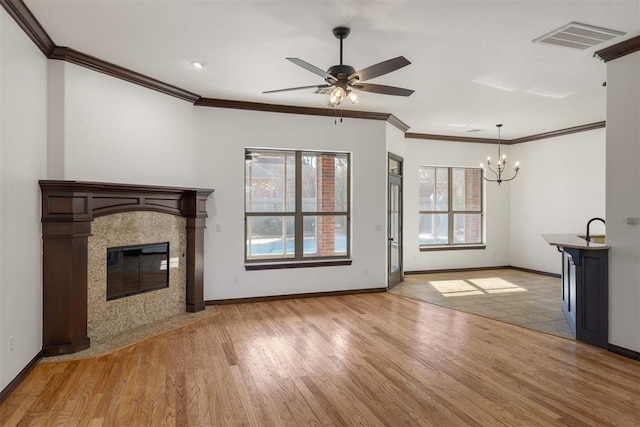 unfurnished living room featuring a tile fireplace, ceiling fan with notable chandelier, a wealth of natural light, and light hardwood / wood-style floors