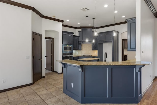 kitchen with light stone counters, hanging light fixtures, stainless steel microwave, ornamental molding, and backsplash