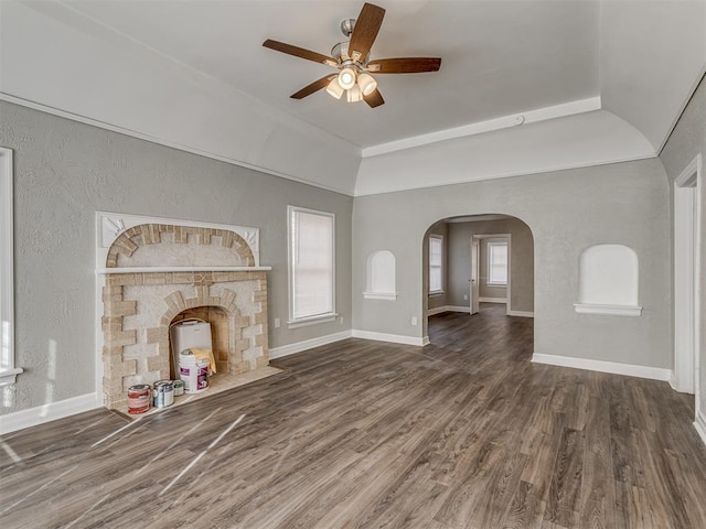 unfurnished living room featuring a stone fireplace, dark hardwood / wood-style floors, and ceiling fan