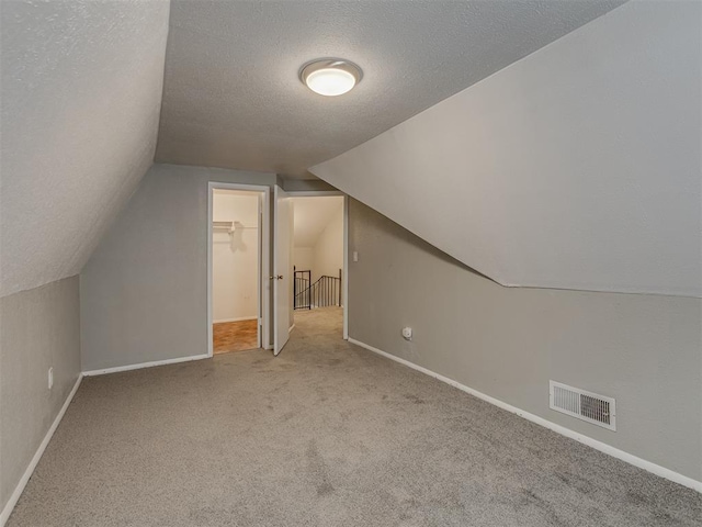 bonus room with vaulted ceiling, light colored carpet, and a textured ceiling