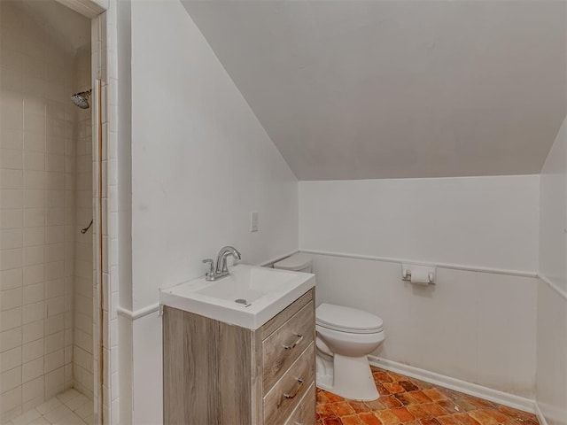 bathroom featuring lofted ceiling, vanity, toilet, and tiled shower