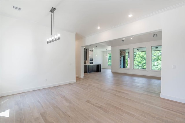 unfurnished living room featuring crown molding, an inviting chandelier, and light hardwood / wood-style flooring