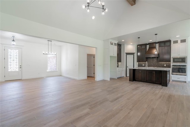 unfurnished living room with beamed ceiling, an inviting chandelier, and light hardwood / wood-style floors