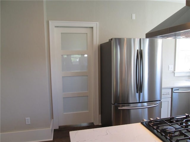 kitchen with appliances with stainless steel finishes, dark hardwood / wood-style floors, white cabinets, light stone countertops, and wall chimney exhaust hood