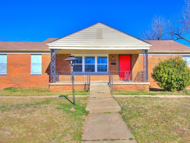 view of front of property featuring a front yard, covered porch, and brick siding