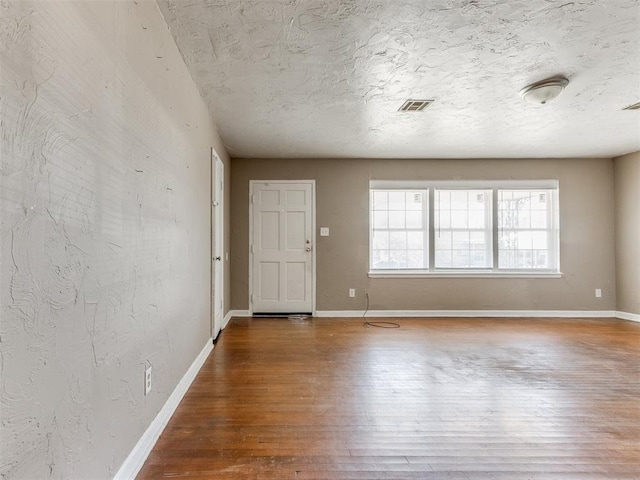 spare room with visible vents, a textured ceiling, baseboards, and wood finished floors