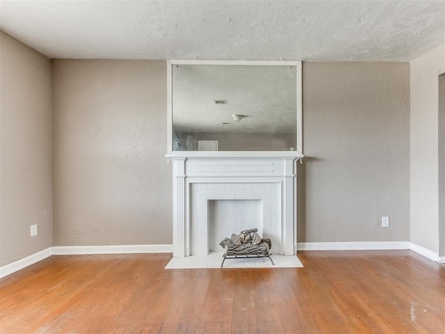 unfurnished living room with a textured ceiling, baseboards, a tiled fireplace, and wood finished floors