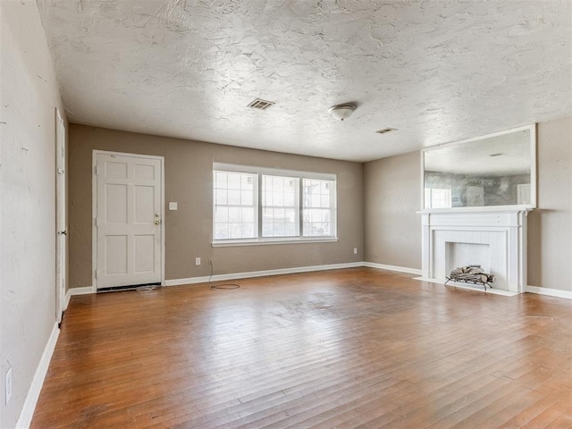 unfurnished living room featuring a fireplace with flush hearth, wood finished floors, visible vents, and baseboards