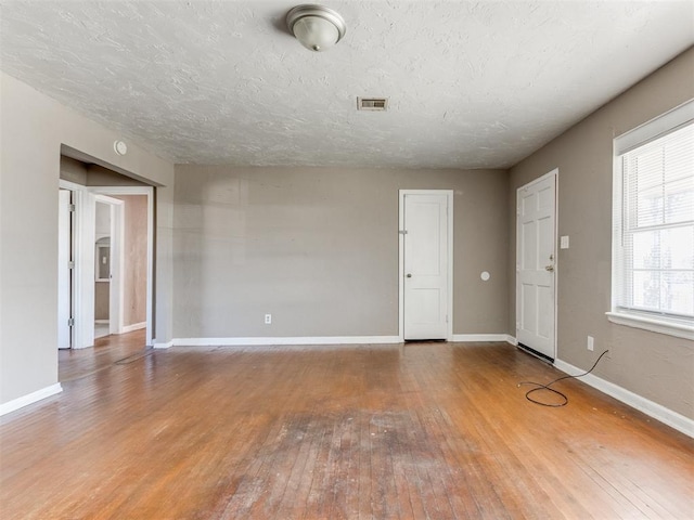 spare room with wood-type flooring, visible vents, a textured ceiling, and baseboards