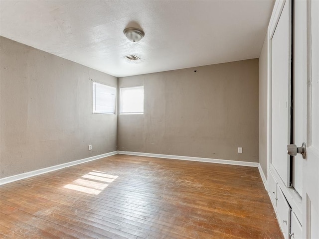 spare room featuring wood-type flooring, visible vents, and baseboards