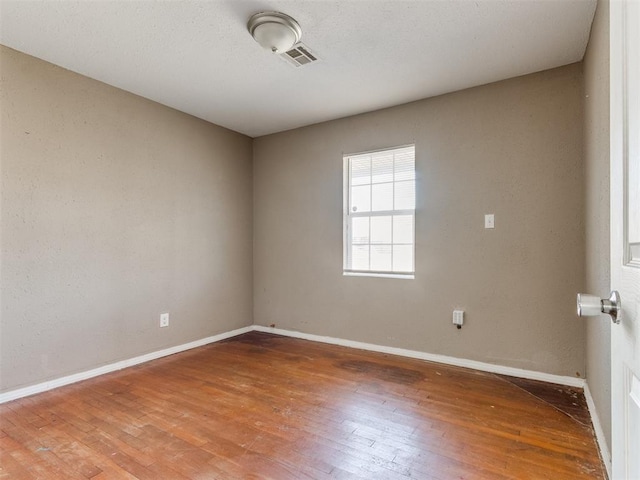 unfurnished room with baseboards, visible vents, and hardwood / wood-style floors