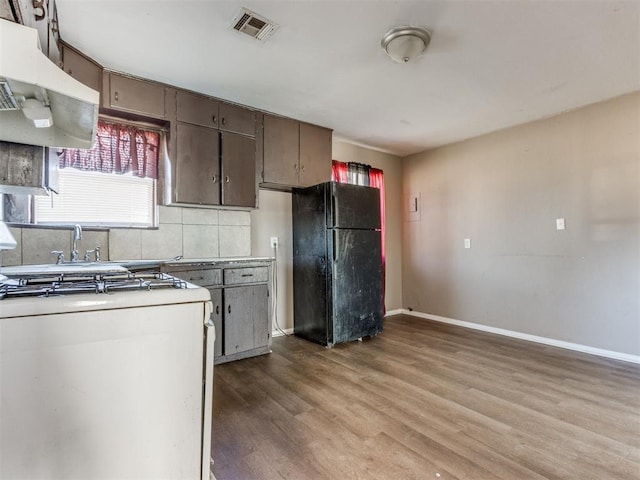 kitchen featuring white range with gas stovetop, wood finished floors, freestanding refrigerator, light countertops, and ventilation hood