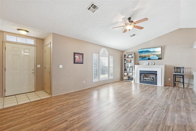 unfurnished living room with lofted ceiling, a textured ceiling, and light wood-type flooring