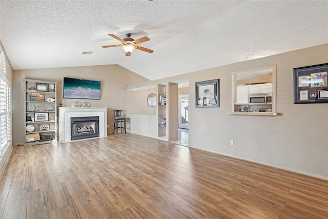 unfurnished living room featuring vaulted ceiling, hardwood / wood-style floors, a textured ceiling, and ceiling fan