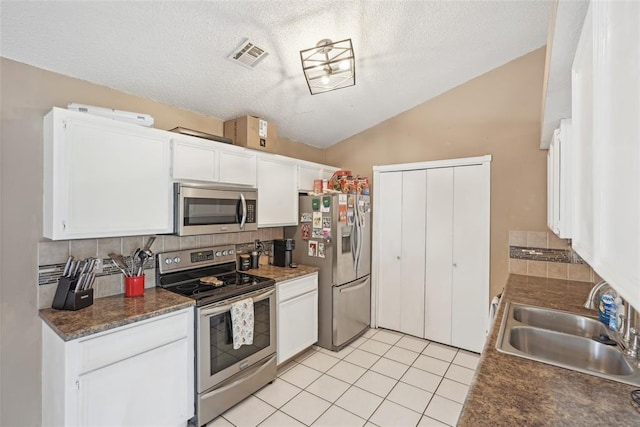 kitchen with sink, appliances with stainless steel finishes, white cabinetry, light tile patterned flooring, and vaulted ceiling