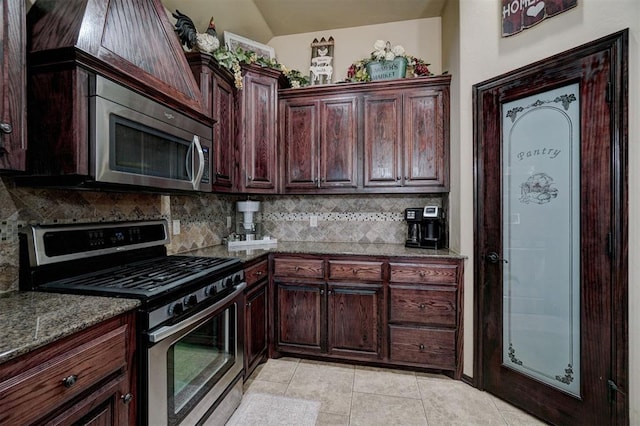 kitchen featuring light tile patterned floors, stainless steel appliances, decorative backsplash, vaulted ceiling, and dark stone counters