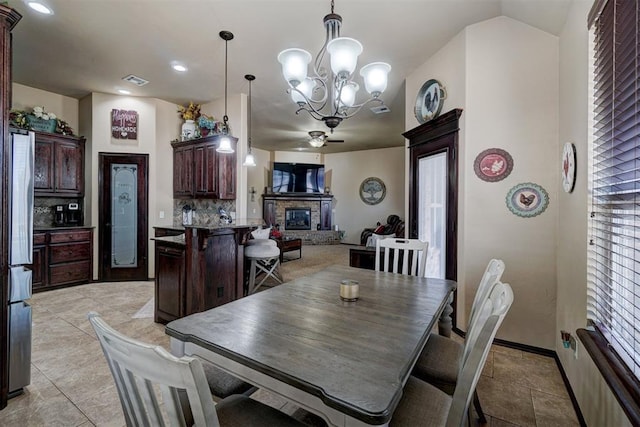 dining area featuring lofted ceiling, ceiling fan with notable chandelier, a fireplace, and light tile patterned floors