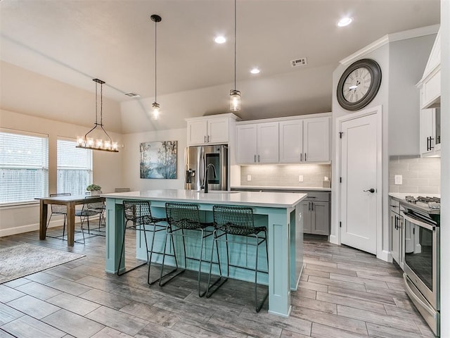 kitchen with appliances with stainless steel finishes, decorative light fixtures, white cabinets, a kitchen breakfast bar, and a kitchen island with sink