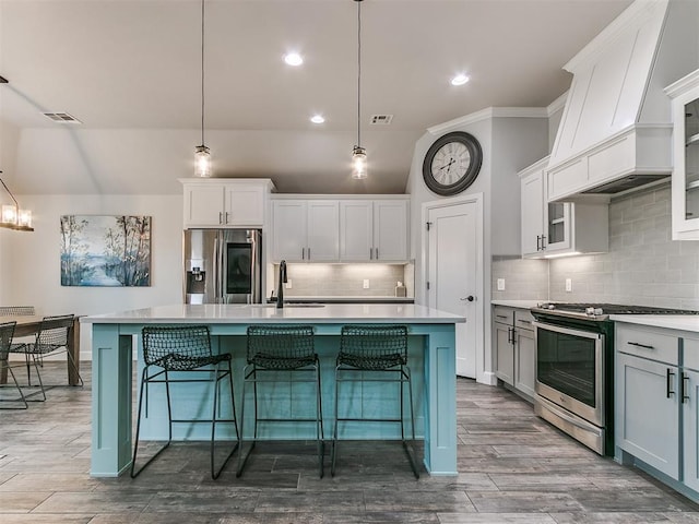 kitchen with white cabinetry, appliances with stainless steel finishes, decorative light fixtures, and a center island with sink