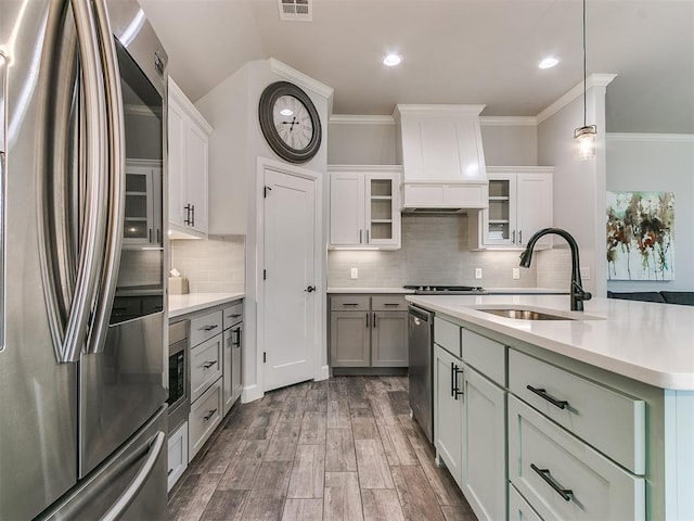 kitchen featuring sink, an island with sink, custom range hood, pendant lighting, and stainless steel appliances