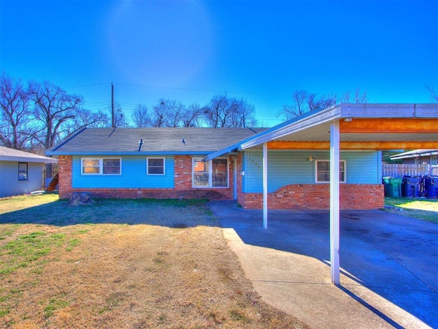 rear view of house featuring an attached carport, concrete driveway, brick siding, and a yard