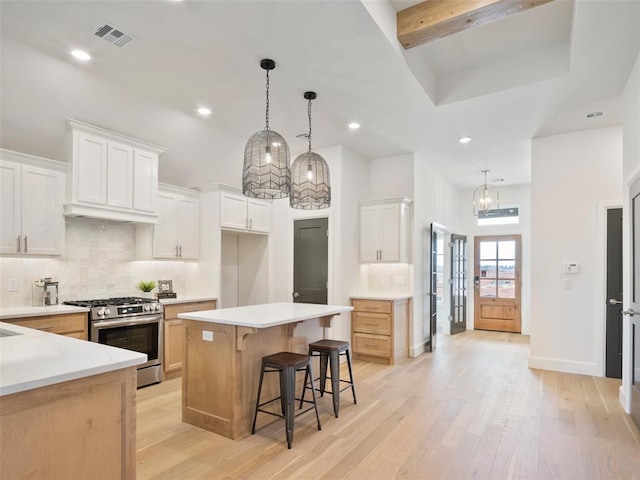 kitchen featuring stainless steel gas range oven, decorative backsplash, visible vents, and light wood-style floors