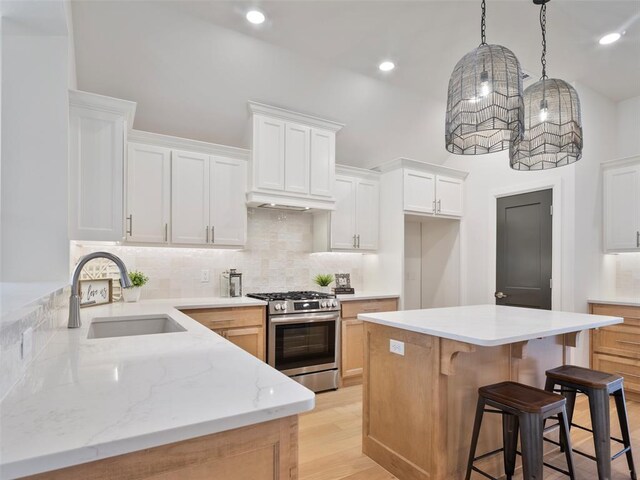 kitchen with a sink, white cabinetry, light wood-type flooring, tasteful backsplash, and gas range