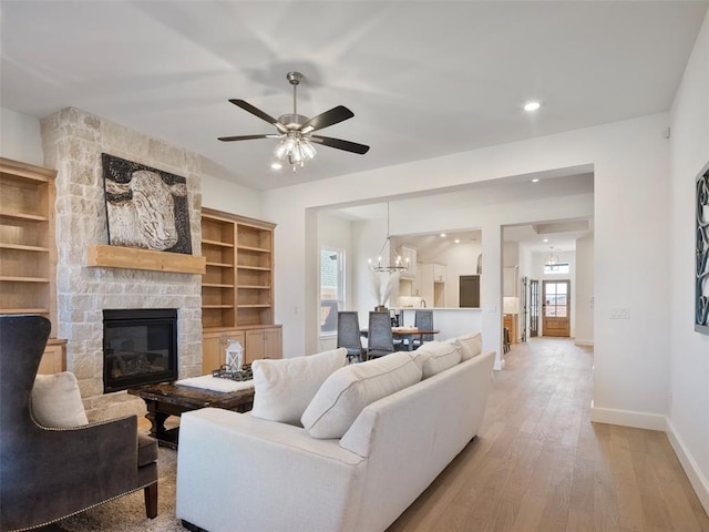 living room featuring recessed lighting, a stone fireplace, wood finished floors, baseboards, and ceiling fan with notable chandelier