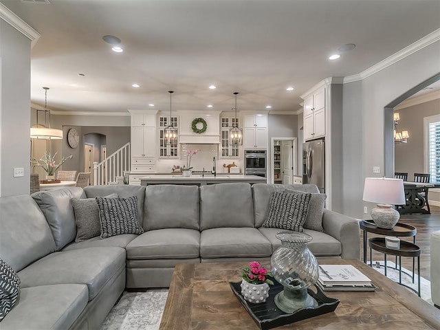 living room with crown molding, wood-type flooring, sink, and a notable chandelier