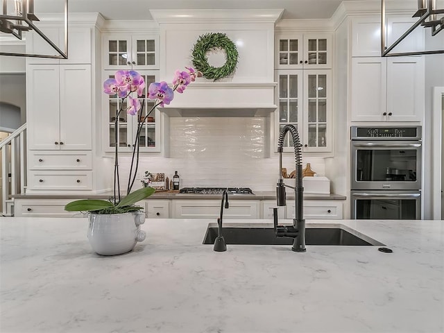 kitchen with pendant lighting, sink, stainless steel appliances, light stone counters, and white cabinets