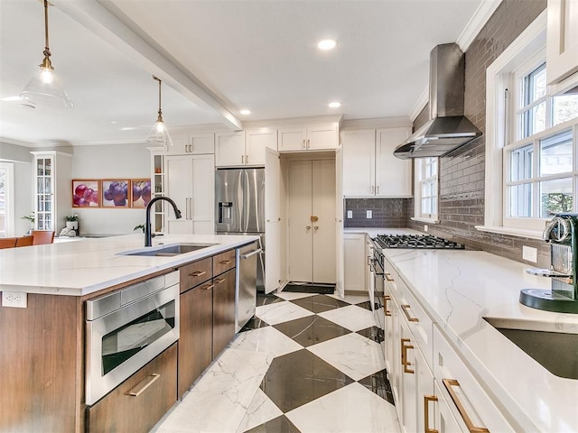 kitchen with an island with sink, sink, white cabinets, hanging light fixtures, and wall chimney exhaust hood