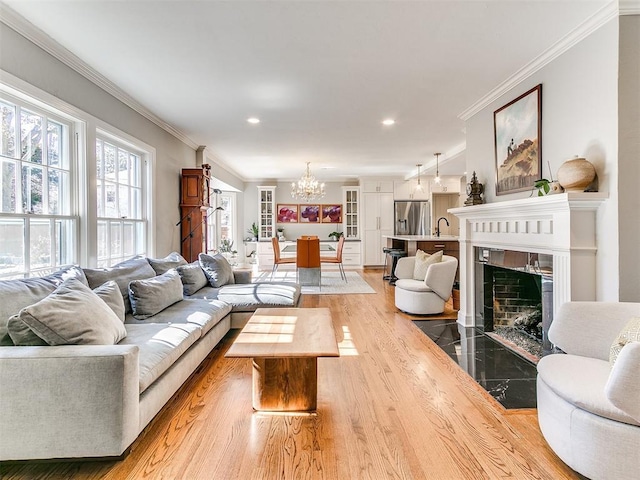 living room featuring sink, crown molding, a chandelier, light wood-type flooring, and a fireplace