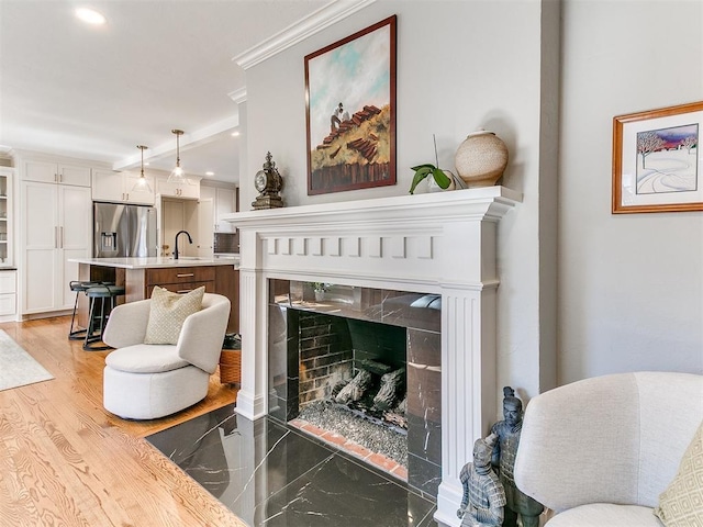 living area featuring crown molding, a high end fireplace, sink, and light hardwood / wood-style flooring