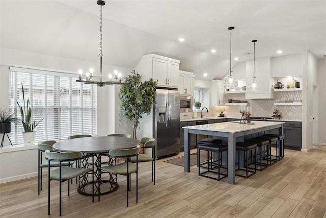 dining space featuring light hardwood / wood-style flooring, sink, vaulted ceiling, and an inviting chandelier