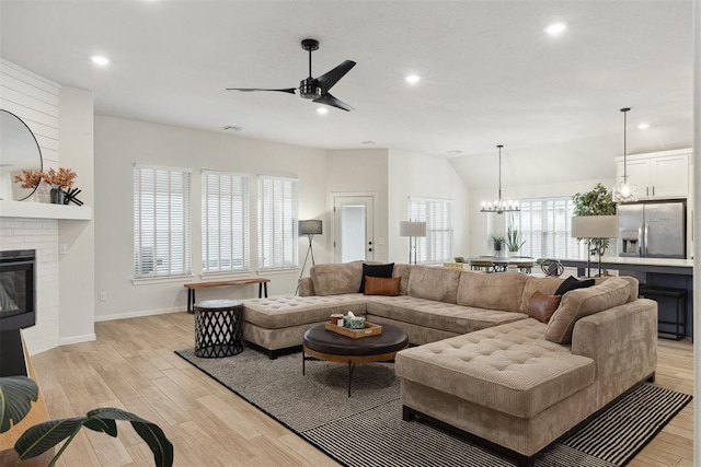 living room featuring vaulted ceiling, ceiling fan with notable chandelier, light hardwood / wood-style floors, and a brick fireplace