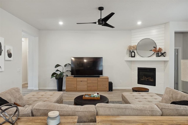 living room with ceiling fan, a large fireplace, and light hardwood / wood-style floors