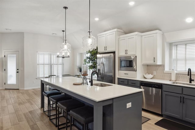 kitchen with stainless steel appliances, an island with sink, sink, and white cabinets