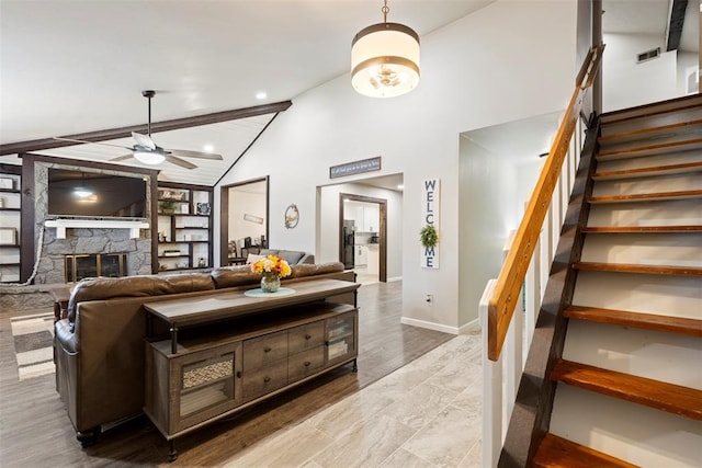 living room with vaulted ceiling with beams, a stone fireplace, ceiling fan, and light wood-type flooring