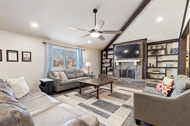 living room with built in features, ceiling fan, vaulted ceiling with beams, a stone fireplace, and light wood-type flooring