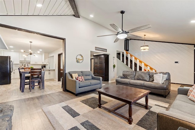 living room with ceiling fan with notable chandelier, vaulted ceiling with beams, sink, and light wood-type flooring