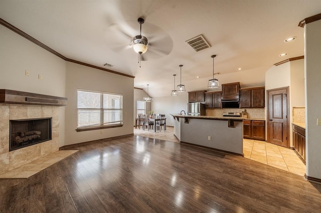 kitchen featuring a breakfast bar area, decorative light fixtures, stainless steel refrigerator, an island with sink, and backsplash