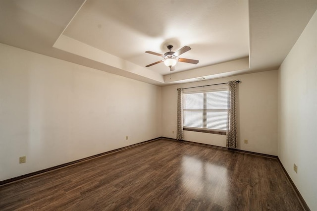 unfurnished room featuring ceiling fan, a tray ceiling, and dark hardwood / wood-style flooring