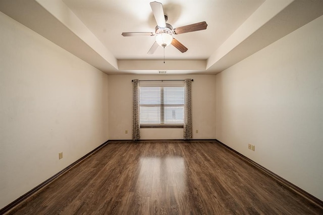 empty room with dark hardwood / wood-style floors, ceiling fan, and a tray ceiling