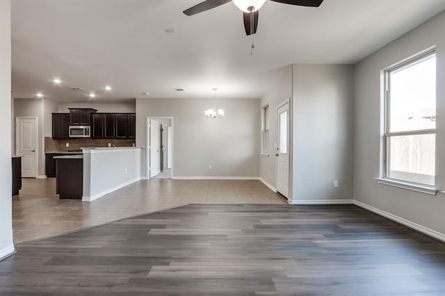 unfurnished living room featuring ceiling fan with notable chandelier and dark tile patterned floors