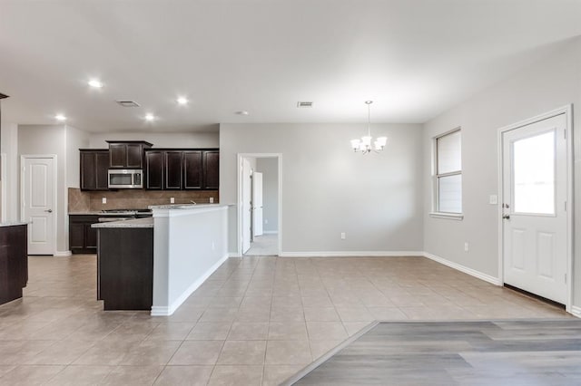 kitchen featuring dark brown cabinetry, an inviting chandelier, hanging light fixtures, light tile patterned floors, and decorative backsplash